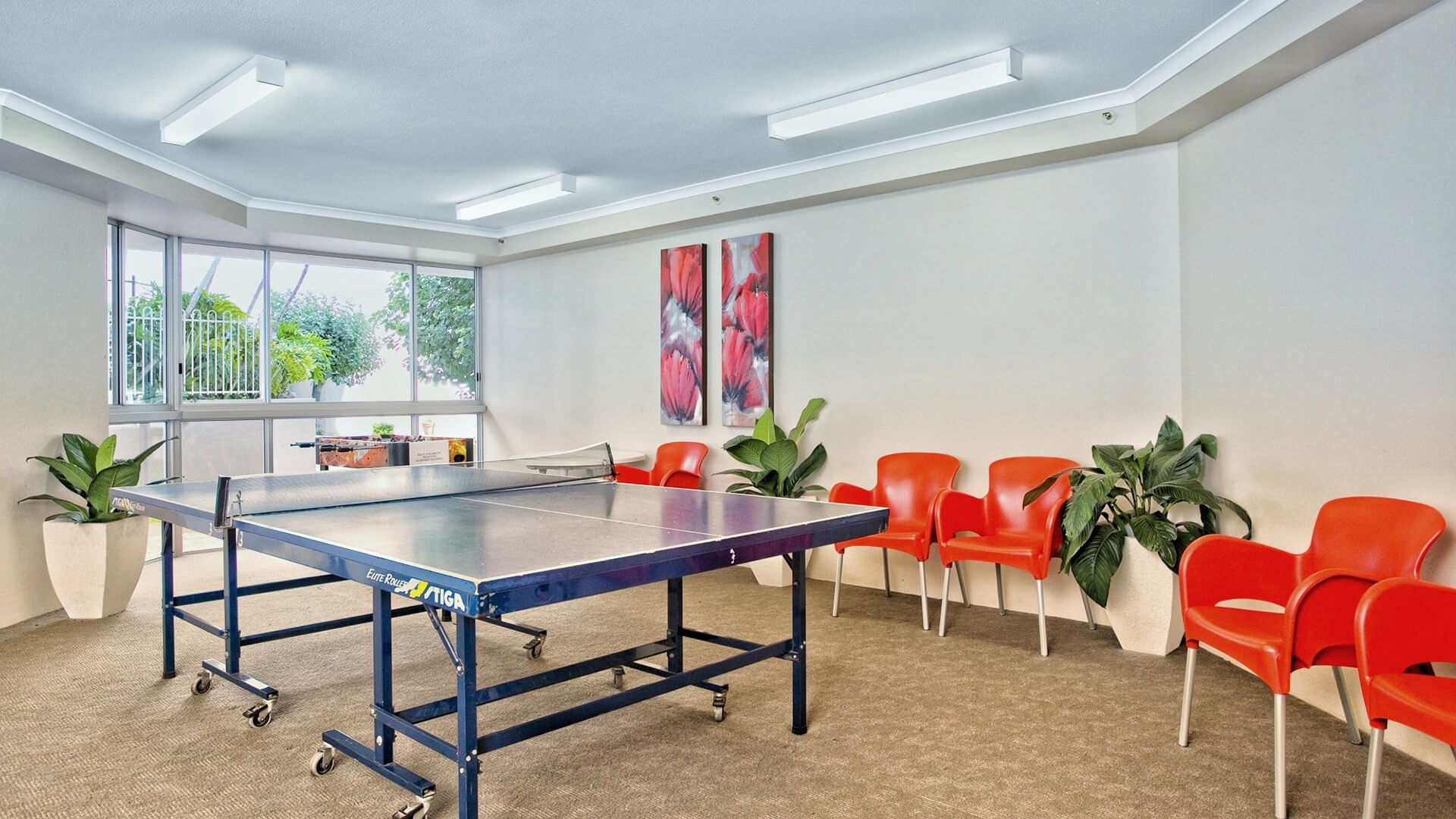 Games room with a table tennis table, red chairs, indoor plants, and large windows at ULTIQA Points North.