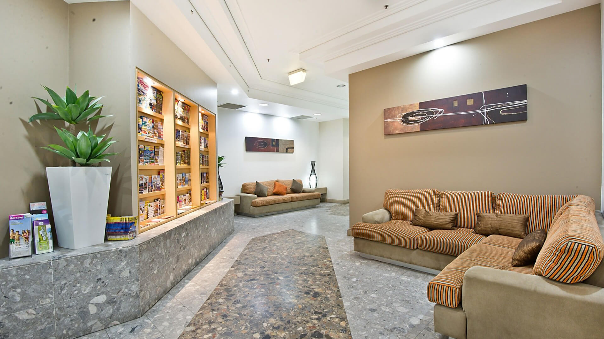 Lobby lounge area at ULTIQA Points North Coolangatta featuring striped sofas, a brochure display wall, modern décor, and tiled flooring.