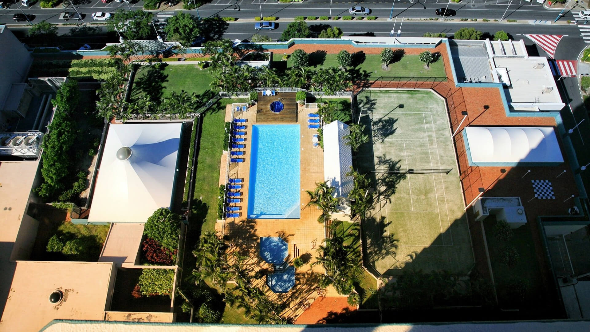 Aerial view of the outdoor facilities, featuring a large swimming pool, spa, sun loungers, tennis court, and landscaped gardens.