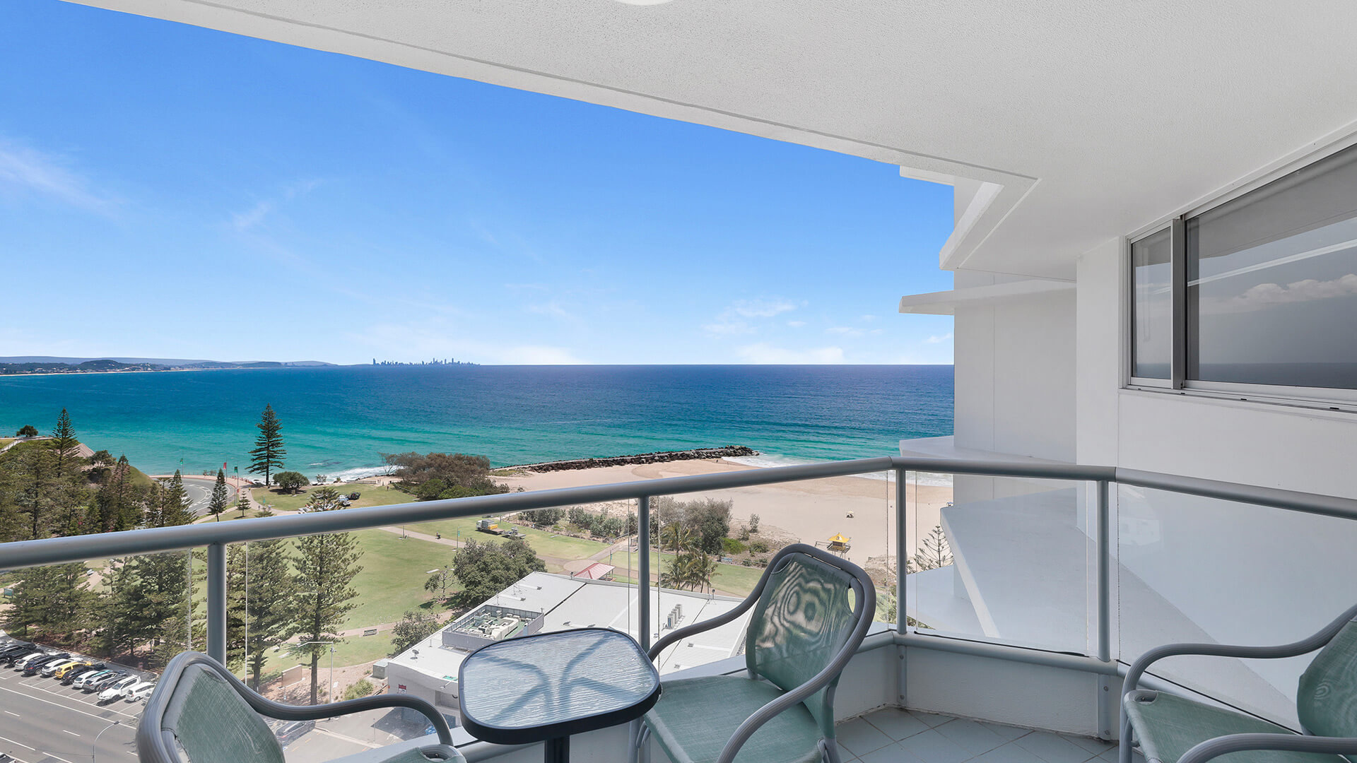 Private balcony with outdoor seating overlooking the beach, ocean, and coastline, offering expansive water and skyline views.