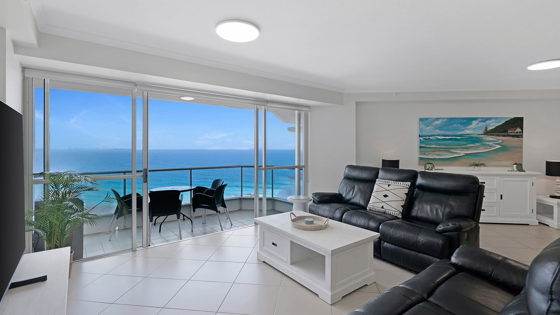 Living area of the 2 Bedroom Superior Ocean View Apartment with black leather recliners, large TV, and balcony access showcasing ocean views.