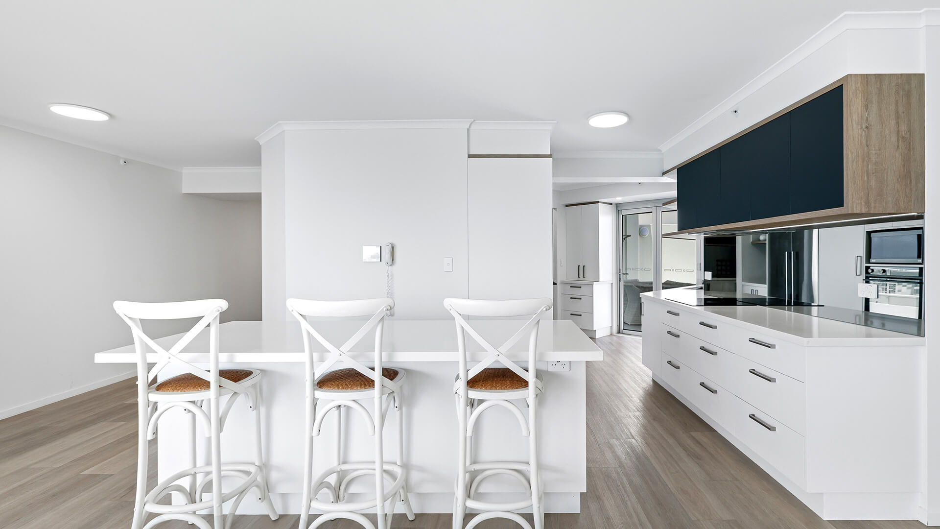 Modern kitchen at the Deluxe 3 Bedroom Ocean View Apartment, featuring a long island bench with bar stools, sleek cabinetry & light timber flooring.