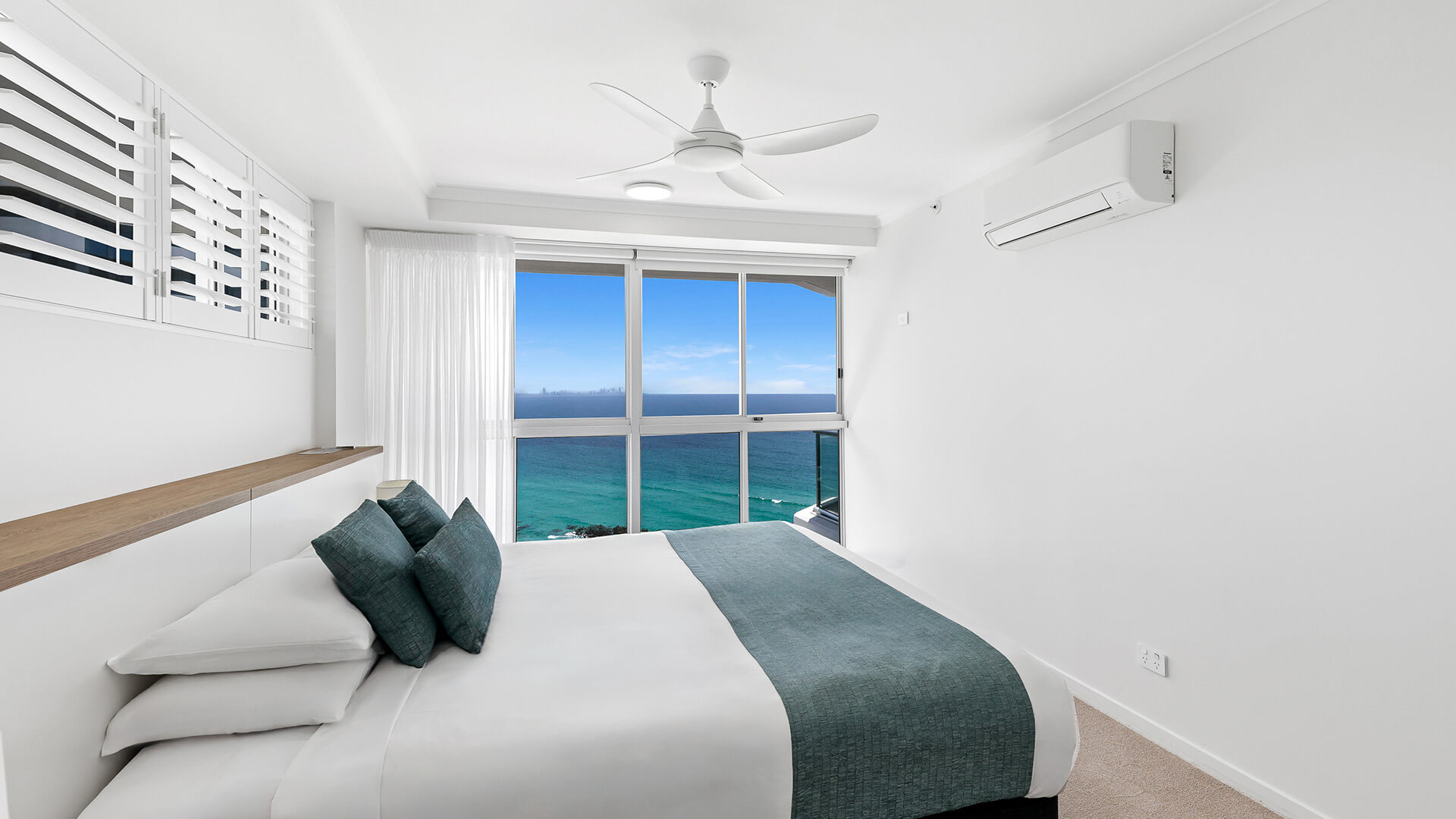Main bedroom in the Deluxe 3 Bedroom Ocean View Apartment, featuring a king bed, coastal décor, & panoramic ocean views from floor-to-ceiling windows.