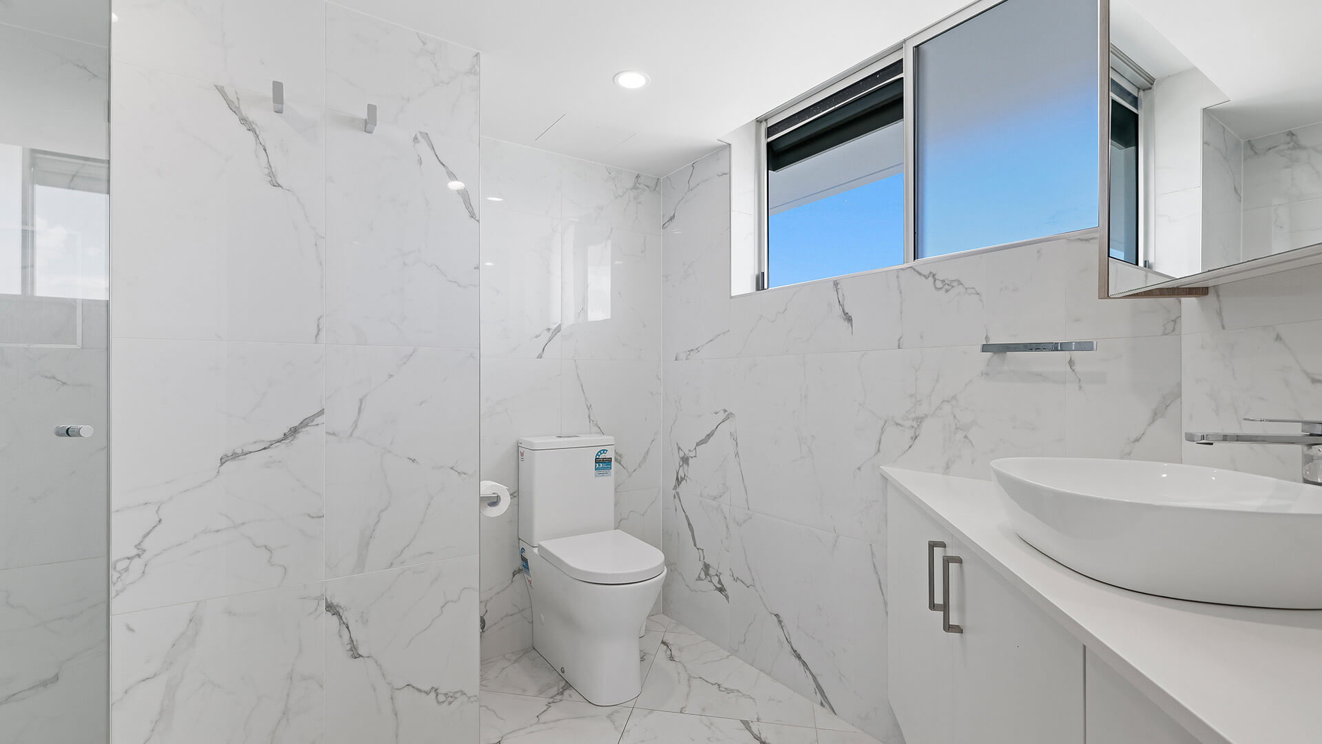 Modern bathroom in the Deluxe 3 Bedroom Ocean View Apartment, featuring marble-look tiles, a walk-in shower, toilet & vanity with a vessel basin.