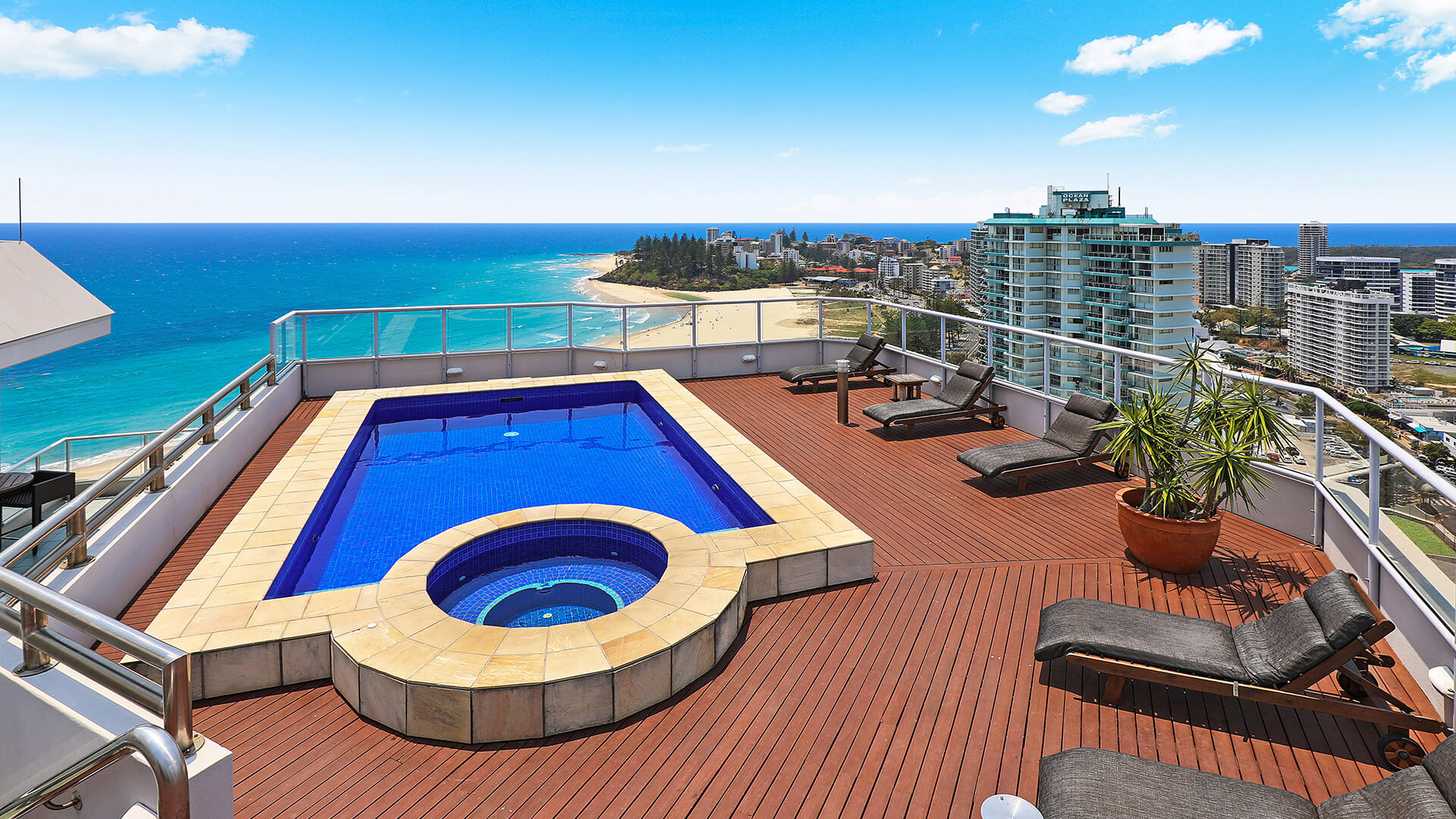 Rooftop pool & spa deck of the 4 Bedroom Oceanfront Penthouse, featuring sun loungers, timber decking, and sweeping ocean and coastline views.