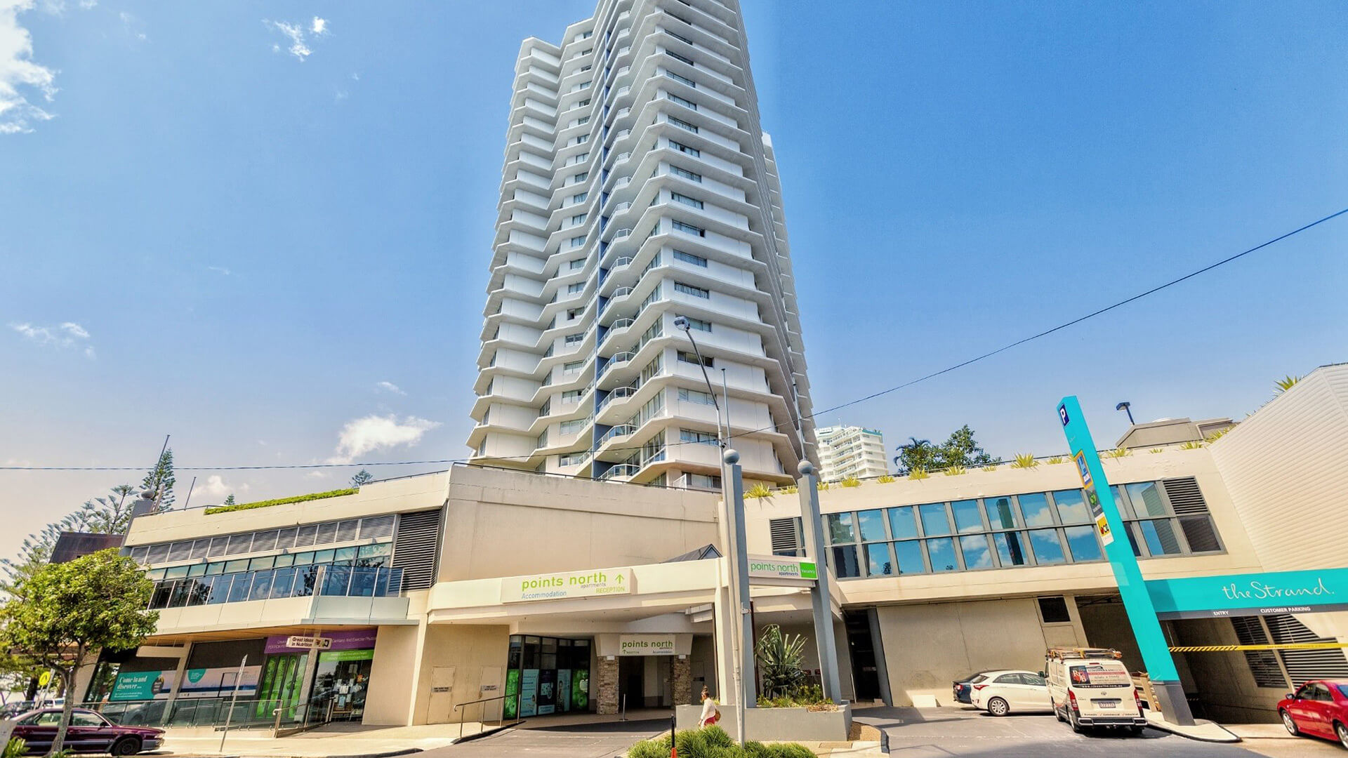 Street-level view of ULTIQA Points North Coolangatta, showcasing the tall white apartment tower above the retail and reception level on Marine Parade.