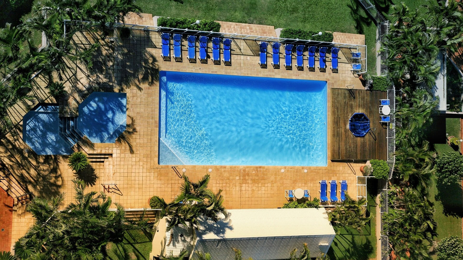 Aerial view of the outdoor pool area, featuring a large rectangular pool, kids’ wading pool, spa deck, sun loungers, and surrounding tropical gardens.