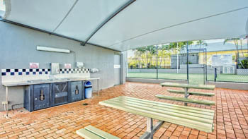 Covered BBQ area with picnic tables overlooking the tennis court at ULTIQA Points North.
