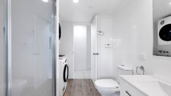Bathroom with laundry facilities in the Superior 2 Bedroom Courtyard Apartment at ULTIQA Points North, featuring a shower and vanity.