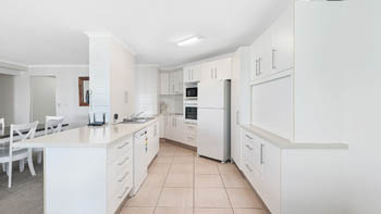 Modern white kitchen in the Superior 2 Bedroom Ocean View Apartment, featuring ample storage, full-size appliances, and a spacious benchtop.