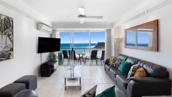Living room in the 2 Bedroom Superior Ocean View Apartment with leather sofas, tropical cushions, wall-mounted TV and ocean-view balcony.