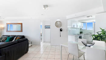 Open-plan living & dining area in a 2 Bedroom Superior Ocean View Apartment with tiled floors, dining set, leather sofa, modern kitchen & ocean views.