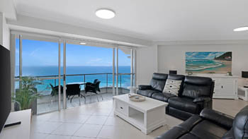 Living area of the 2 Bedroom Superior Ocean View Apartment with black leather recliners, large TV, and balcony access showcasing ocean views.