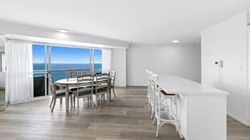 Dining area & kitchen with bar seating in a Deluxe 3 Bedroom Ocean View Apartment, featuring expansive ocean views from the balcony.