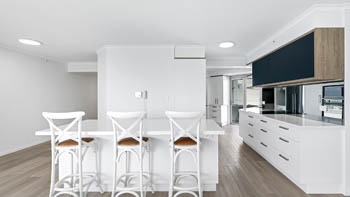 Modern kitchen at the Deluxe 3 Bedroom Ocean View Apartment, featuring a long island bench with bar stools, sleek cabinetry & light timber flooring.
