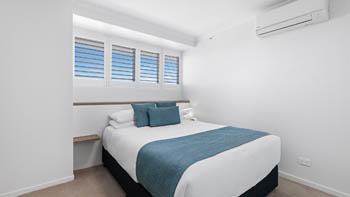 Bedroom in the Deluxe 3 Bedroom Ocean View Apartment at ULTIQA Points North, featuring a queen bed with teal accents and shuttered windows.