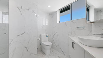 Modern bathroom in the Deluxe 3 Bedroom Ocean View Apartment, featuring marble-look tiles, a walk-in shower, toilet & vanity with a vessel basin.