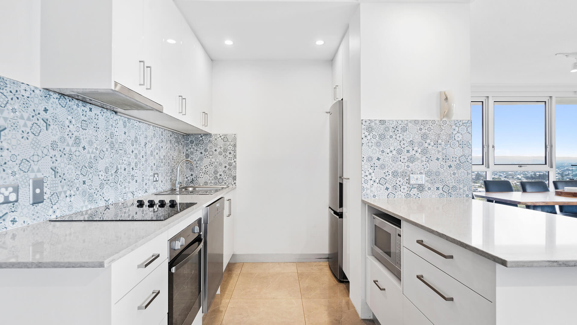 Modern white kitchen with a blue tile backsplash. Fully equipped with oven, stove, microwave and a lot of storage at ULTIQA Beach Haven.