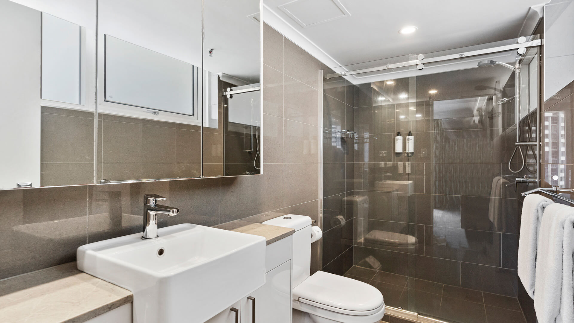 Bathroom with stone tiles, white sink, toilet and a walk-in shower at ULTIQA Beach Haven.