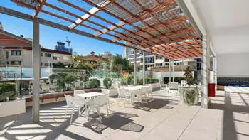 Outdoor dining area at ULTIQA Beach Haven on Broadbeach featuring modern white tables and chairs, shaded by a timber pergola with hanging lights.