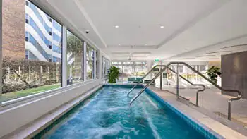 Indoor spa with bubbling jets at ULTIQA Beach Haven on Broadbeach, featuring floor-to-ceiling windows, stainless steel handrails and poolside lounge seating for ultimate relaxation.