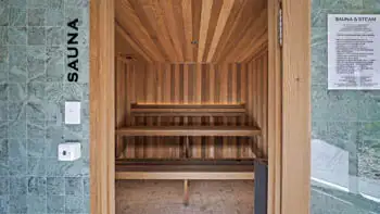 Modern cedar-lined sauna at ULTIQA Beach Haven on Broadbeach, featuring tiered bench seating, tiled entrance wall and wellness guidelines for a rejuvenating relaxation experience.