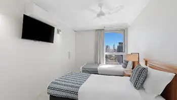 Second bedroom in the 2 Bedroom Ocean View Apartment at ULTIQA Beach Haven on Broadbeach with two single beds, TV, and city views.