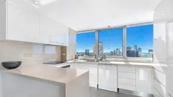 Modern fully equipped kitchen in the 2 Bedroom Ocean View Apartment at ULTIQA Beach Haven on Broadbeach featuring sleek white cabinetry, stone benchtops, and city skyline views through large windows.