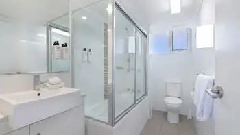 Bright bathroom at ULTIQA Beach Haven on Broadbeach featuring a shower-over-bath, modern vanity, toilet, and complimentary amenities.