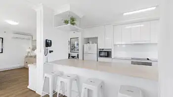 Spacious kitchen with white cabinetry, full-size fridge, and breakfast bar seating in the Standard 2 Bedroom Ocean View Apartment at ULTIQA Beach Haven on Broadbeach.