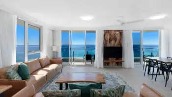 Spacious oceanfront living area with leather lounges, coastal décor, dining area, and floor-to-ceiling doors to uninterrupted beach views.