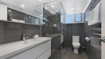 Modern featuring a glass-enclosed rainfall shower, sleek vanity, and dark floor-to-ceiling tiles.
