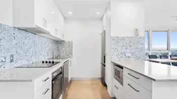 Modern white kitchen with a blue tile backsplash. Fully equipped with oven, stove, microwave and a lot of storage at ULTIQA Beach Haven on Broadbeach.