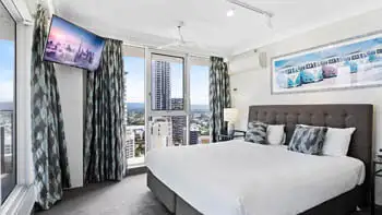 Master bedroom with dark headrest, whit plush bedding and a view of the Gold Coast at ULTIQA Beach Haven on Broadbeach.