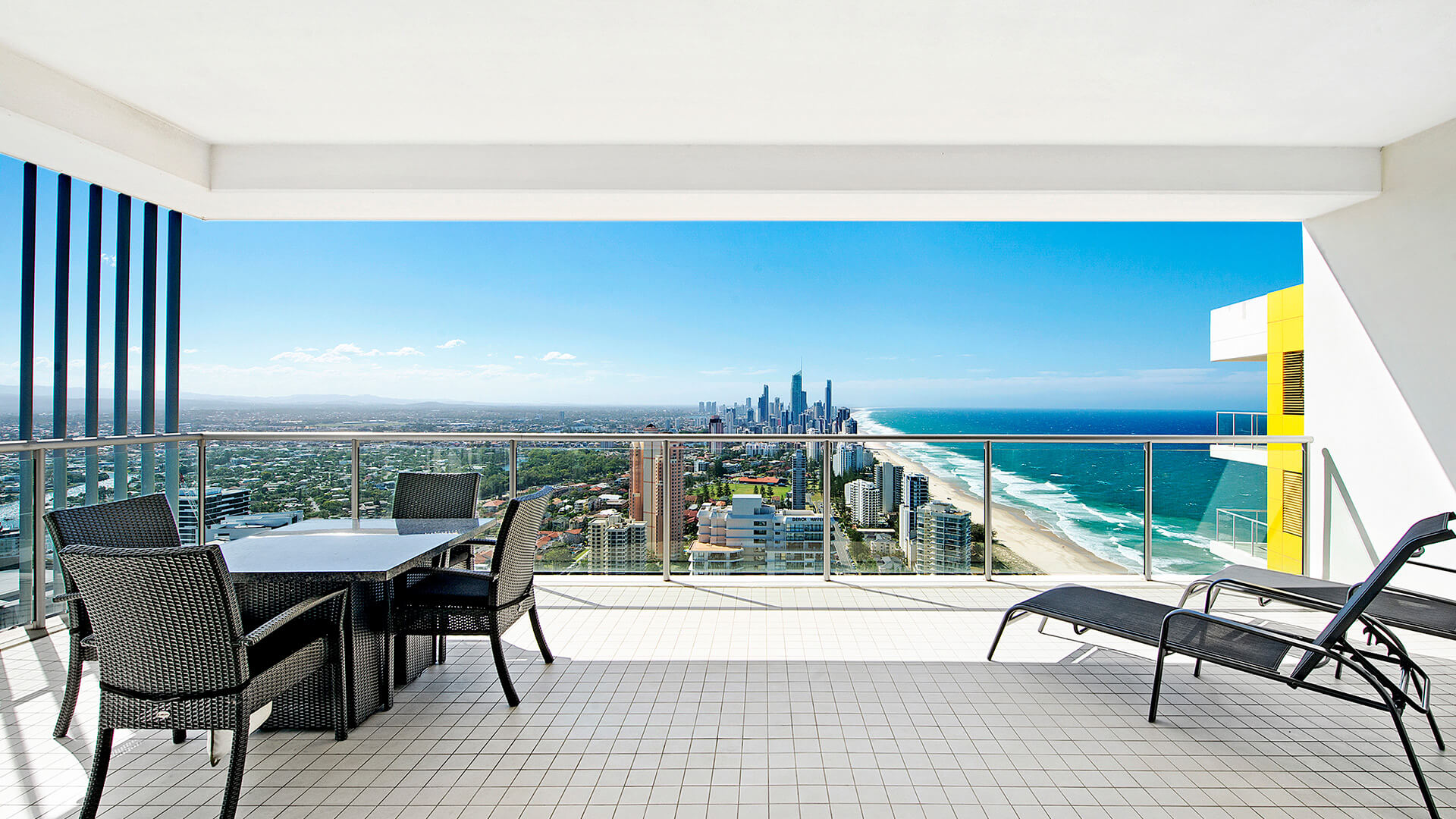 Private balcony with outdoor dining and sun loungers, overlooking Surfers Paradise and the coastline from the 2 Bedroom Gold Coast View Suite at ULTIQA Air on Broadbeach.