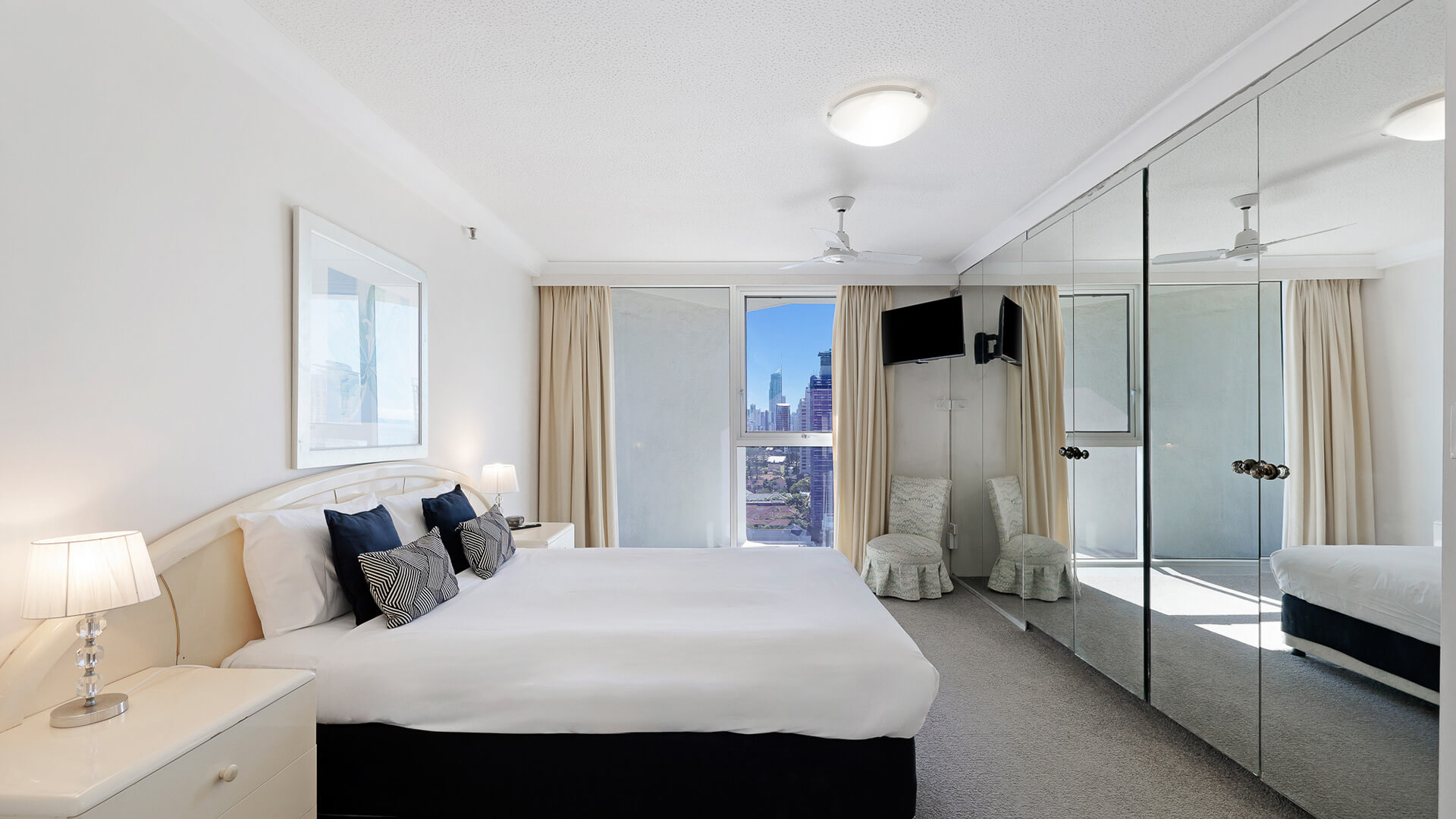 Main bedroom in the Standard 2 Bedroom Ocean View Apartment at ULTIQA Beach Haven, featuring a king bed, mirrored wardrobes, and city skyline views.