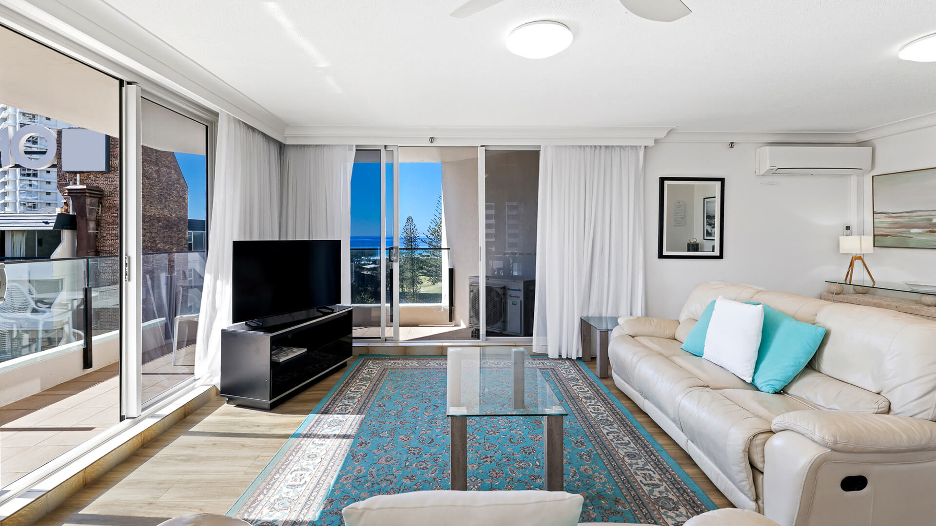 Living room with ocean views at ULTIQA Beach Haven’s Standard 2 Bedroom Ocean View Apartment, featuring leather lounges, a flat-screen TV, and natural light. 