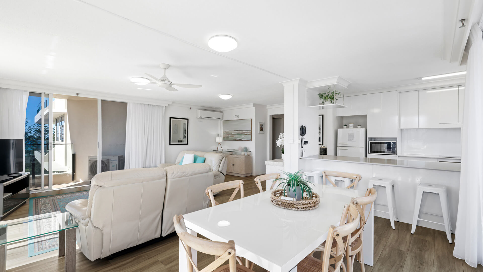 Open-plan living, dining, and kitchen area in ULTIQA Beach Haven’s Standard 2 Bedroom Ocean View Apartment, featuring modern furnishings, a white interior, and natural light.