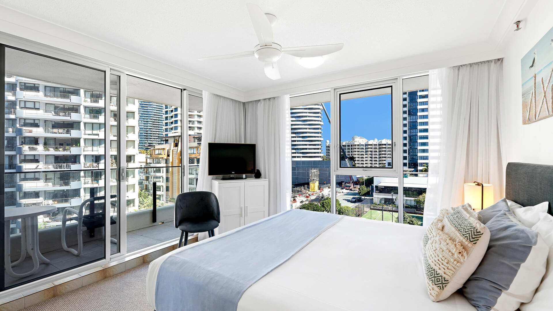 Master bedroom in the Standard 2 Bedroom Ocean View Apartment at ULTIQA Beach Haven, featuring a comfortable bed, ceiling fan, and large windows with city views.