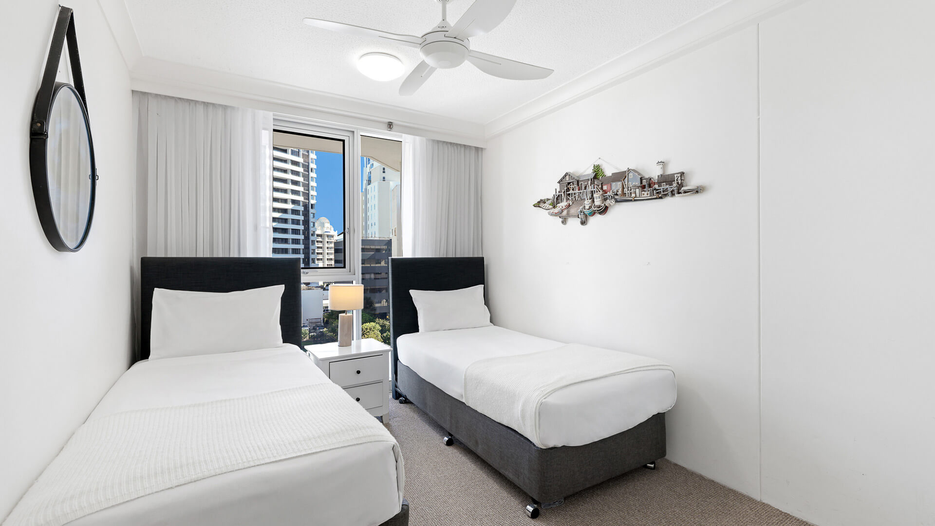 Second bedroom in the Standard 2 Bedroom Ocean View Apartment at ULTIQA Beach Haven, featuring two single beds, ceiling fan, and city views.