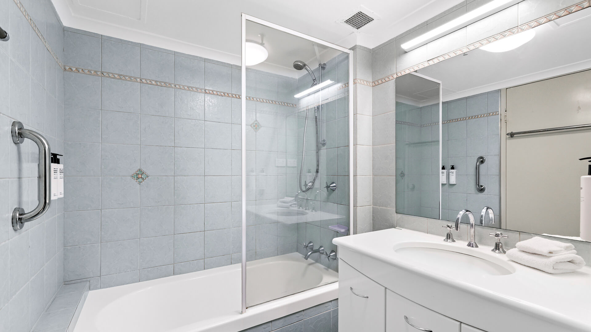 Main bathroom in the Standard 2 Bedroom Ocean View Apartment at ULTIQA Beach Haven, featuring a combined shower and bathtub, large mirror, and tiled walls.