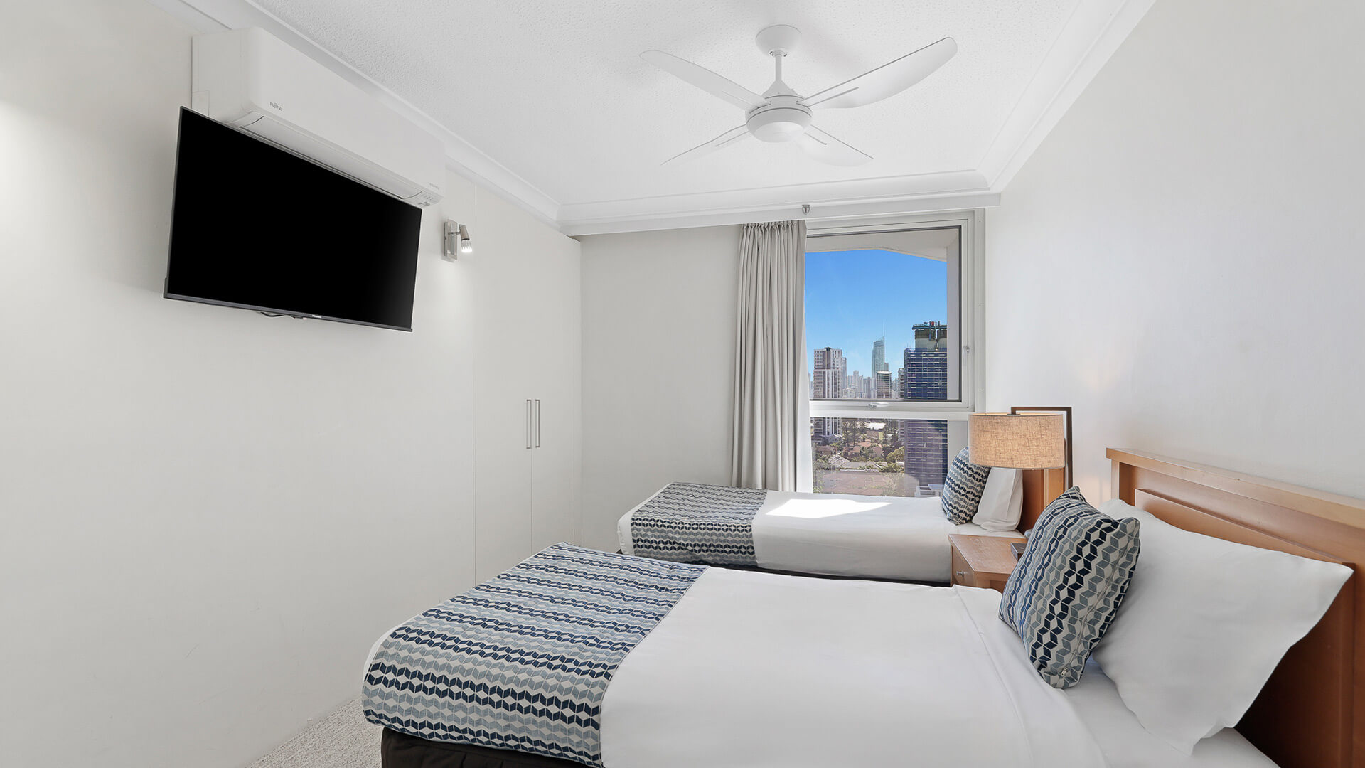 Second bedroom in the 2 Bedroom Ocean View Apartment at ULTIQA Beach Haven with two single beds, TV, and city views.