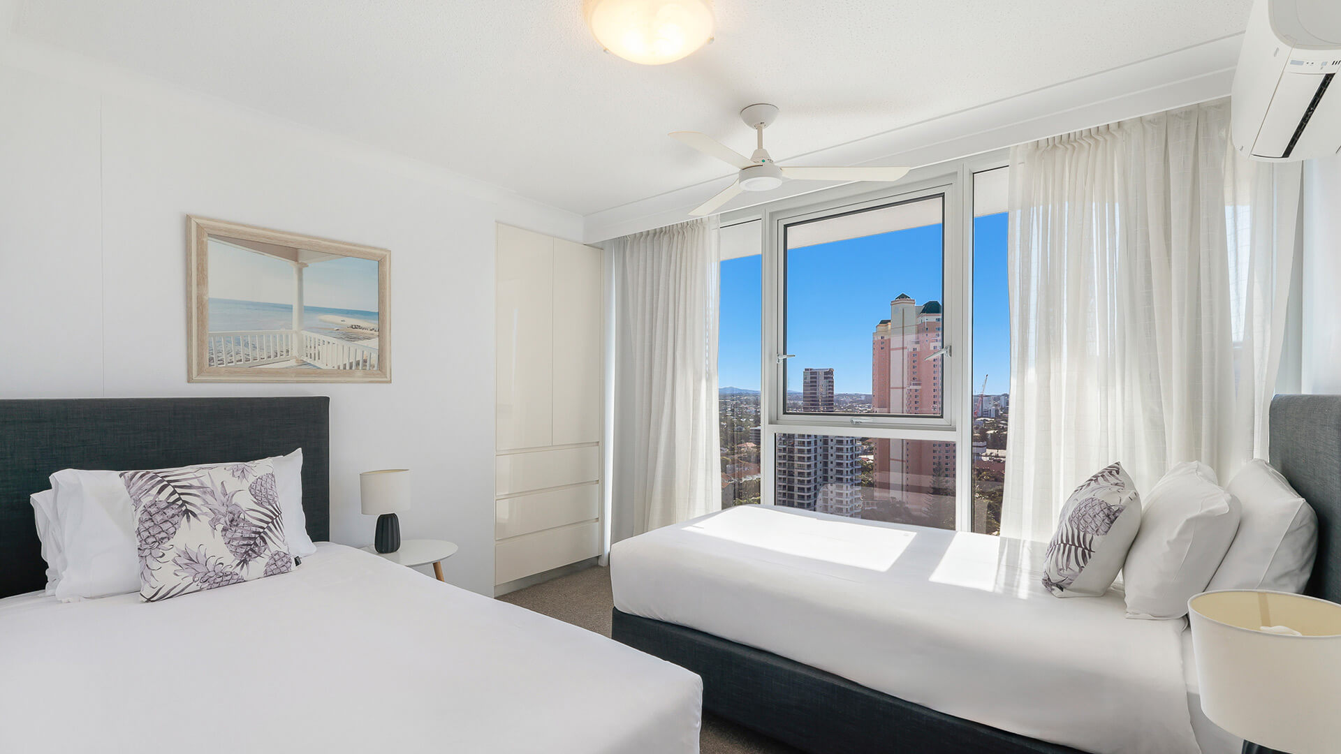 Bright and airy second bedroom in the 2 Bedroom Ocean View Apartment at ULTIQA Beach Haven featuring a queen and single bed, city views, and modern furnishings.