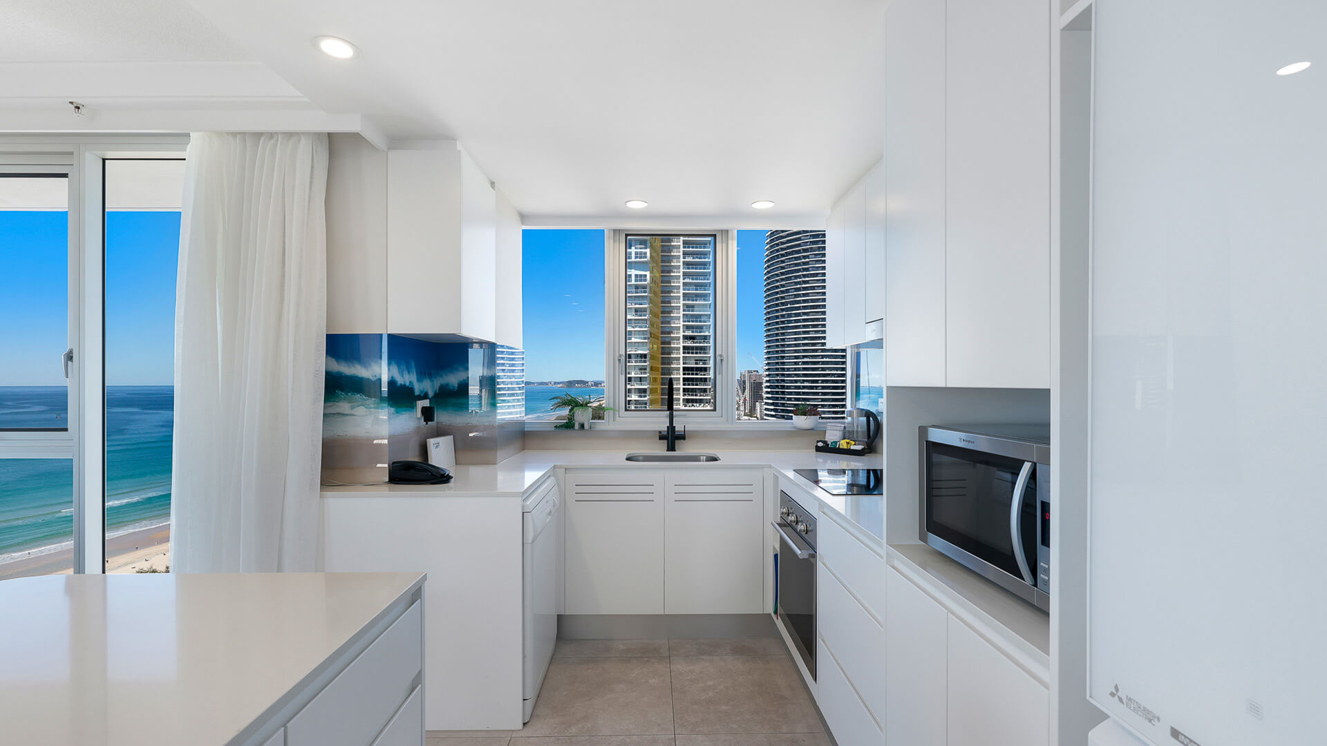 Contemporary, featuring sleek white cabinetry, modern appliances, and city views framed by floor-to-ceiling windows.