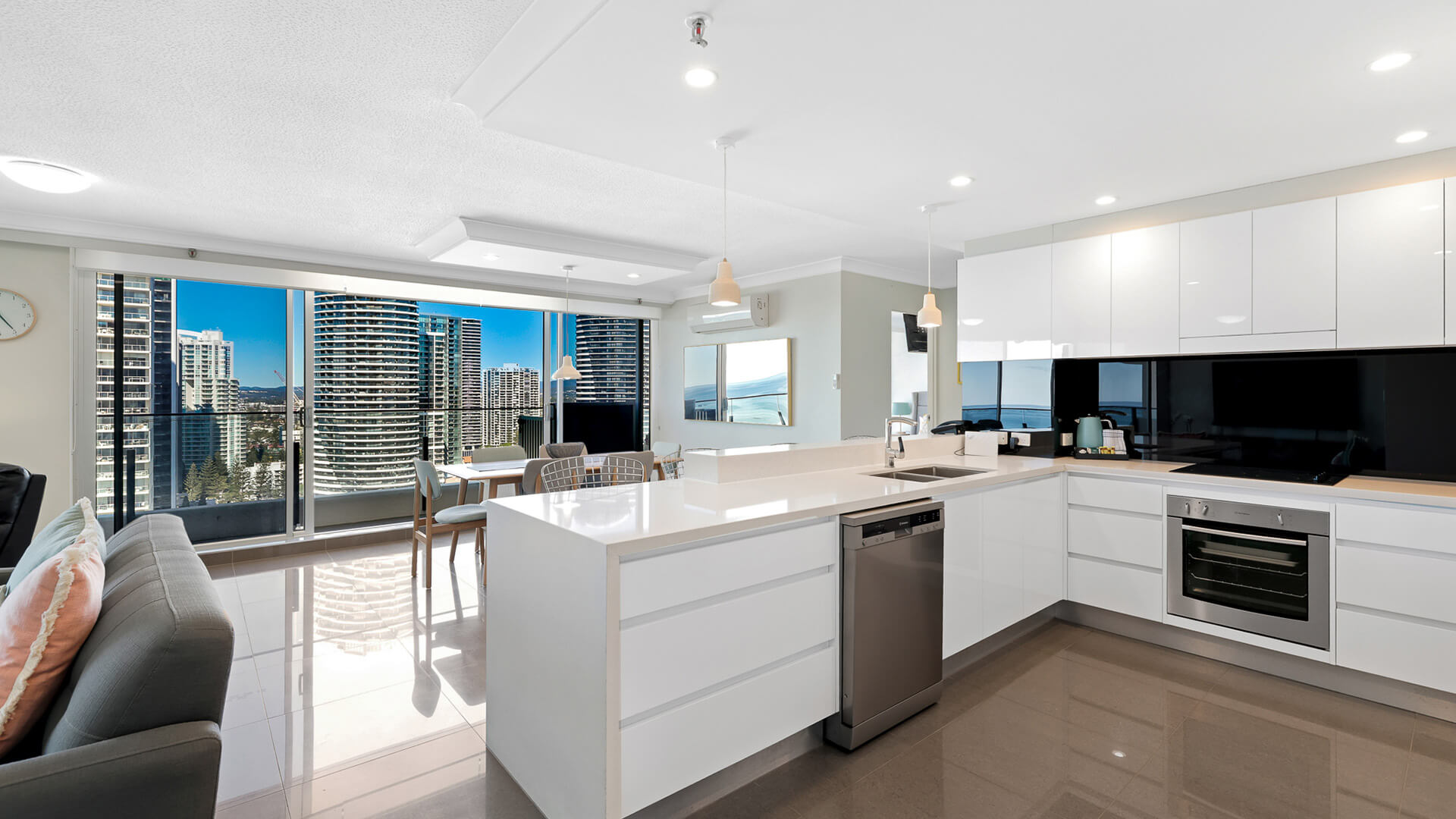 Open-plan kitchen and living with floor-to-ceiling windows, ocean glimpses, and city skyline views.