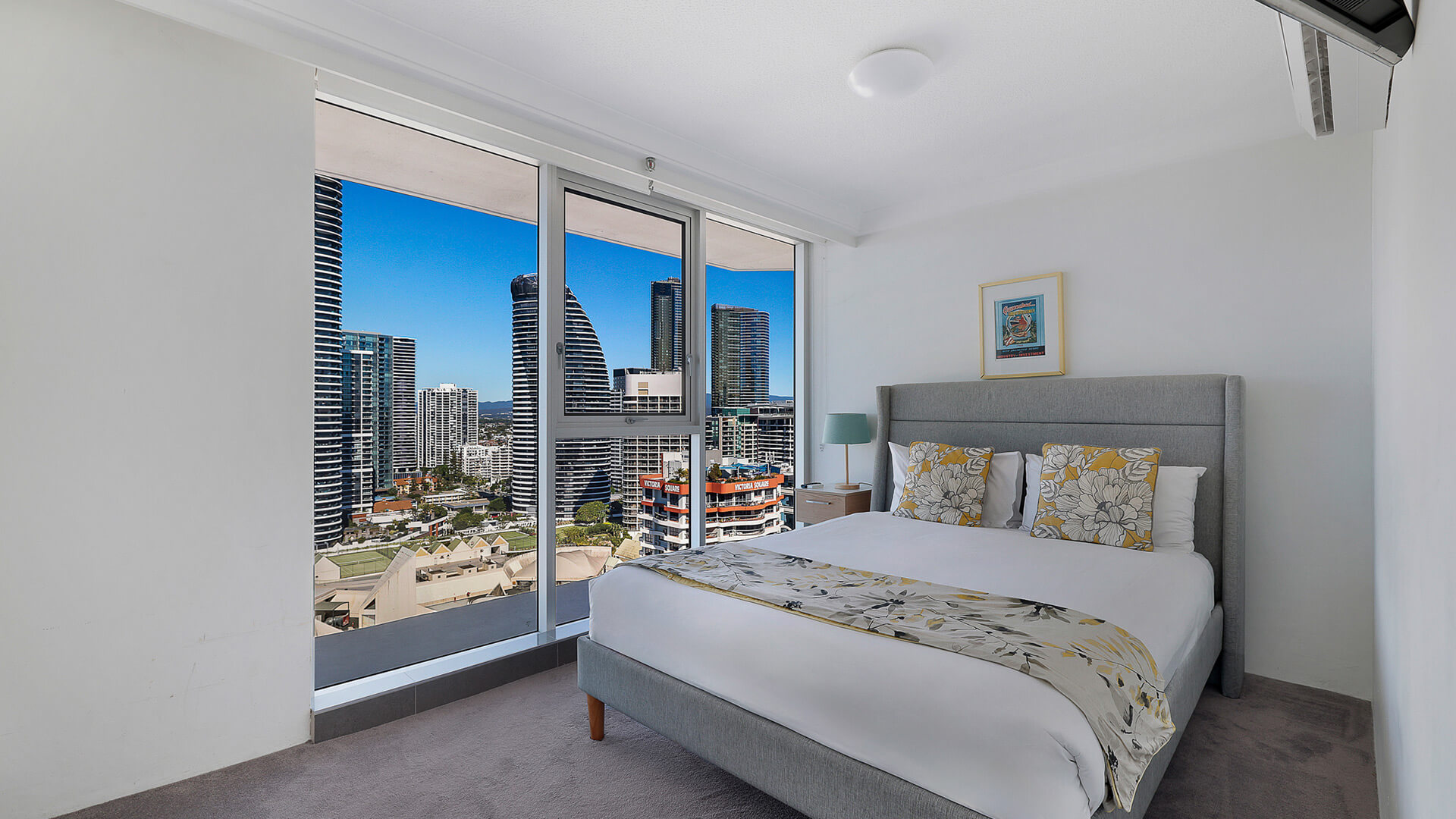 Bedroom with a plush queen bed, coastal-inspired decor, and skyline views through floor-to-ceiling windows.