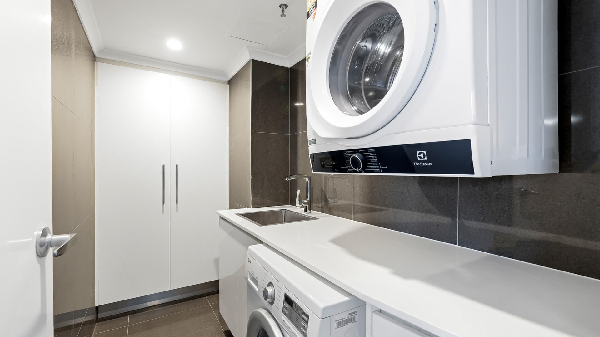 In-apartment laundry featuring Electrolux appliances, a washing machine, dryer, sink, and built-in storage for convenient self-contained stays.