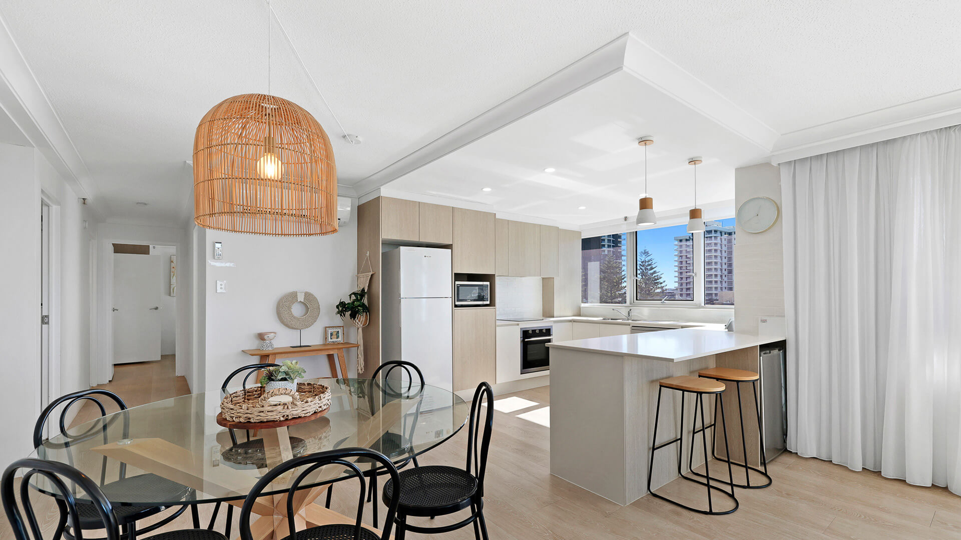 Bright open-plan dining and kitchen featuring coastal décor, modern appliances, breakfast island, and city views through large windows.