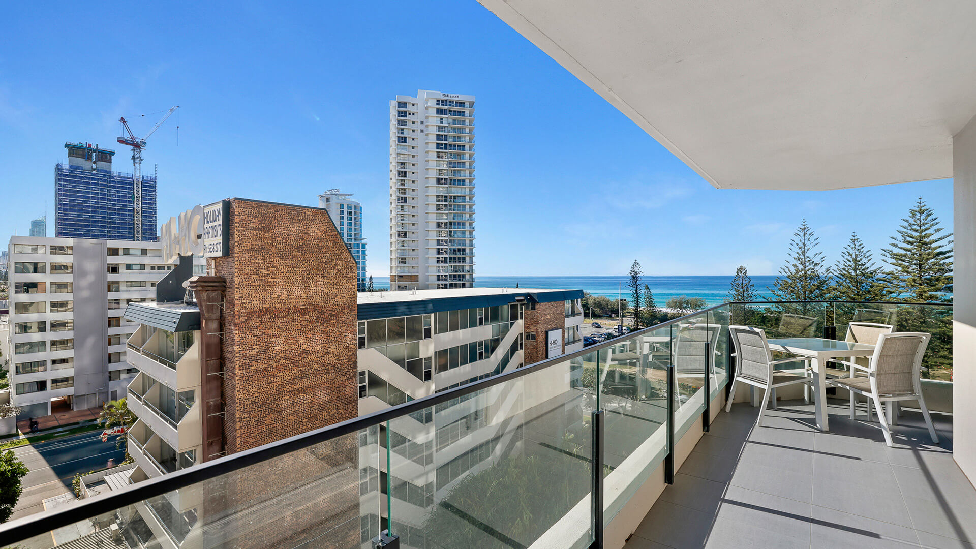 Spacious balcony featuring ocean views, an outdoor dining table, and a glass balustrade overlooking the pool and Broadbeach skyline.