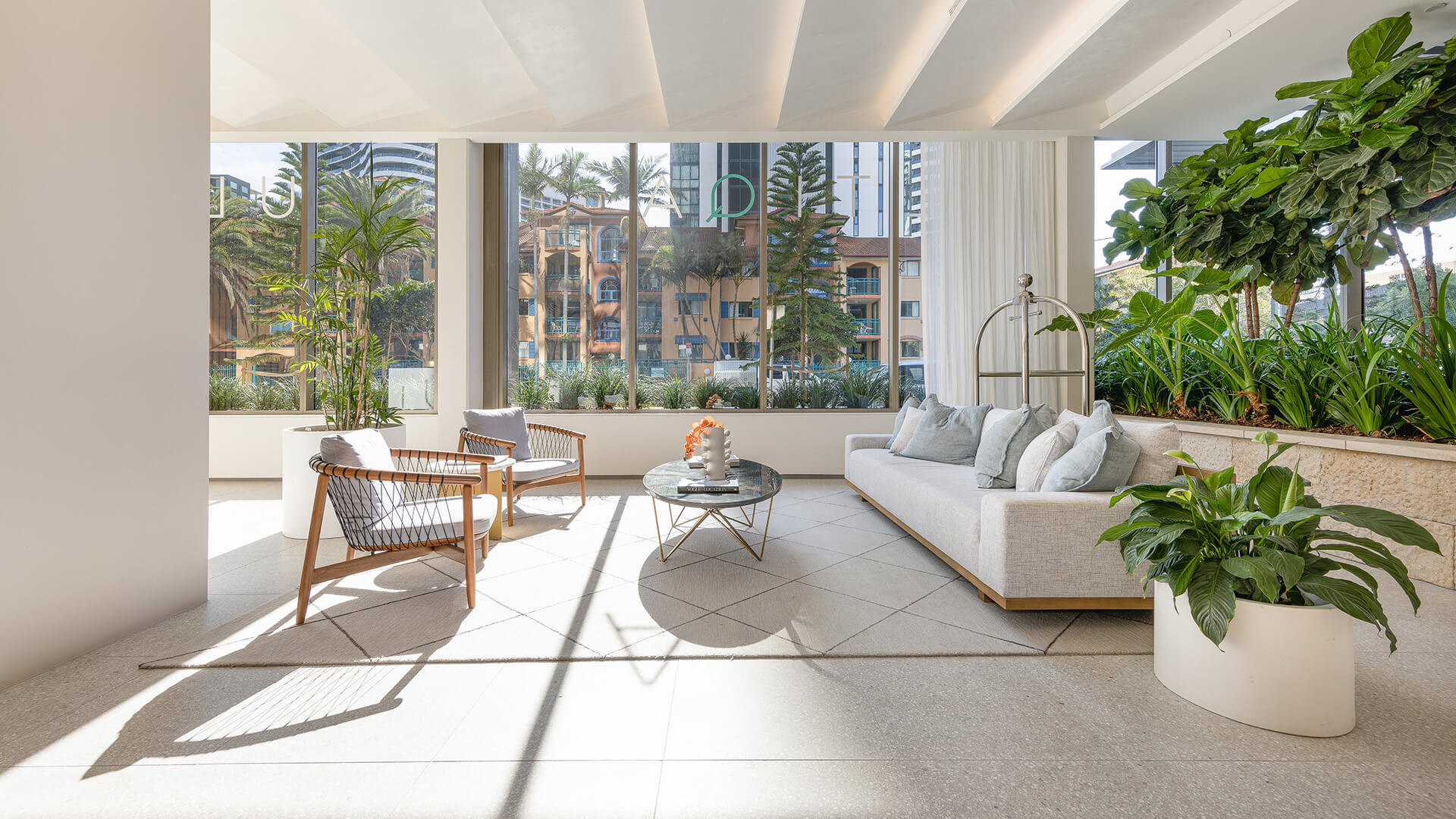 Bright and modern ULTIQA Signature lobby with large windows, indoor plants, comfortable seating, and natural light streaming in.